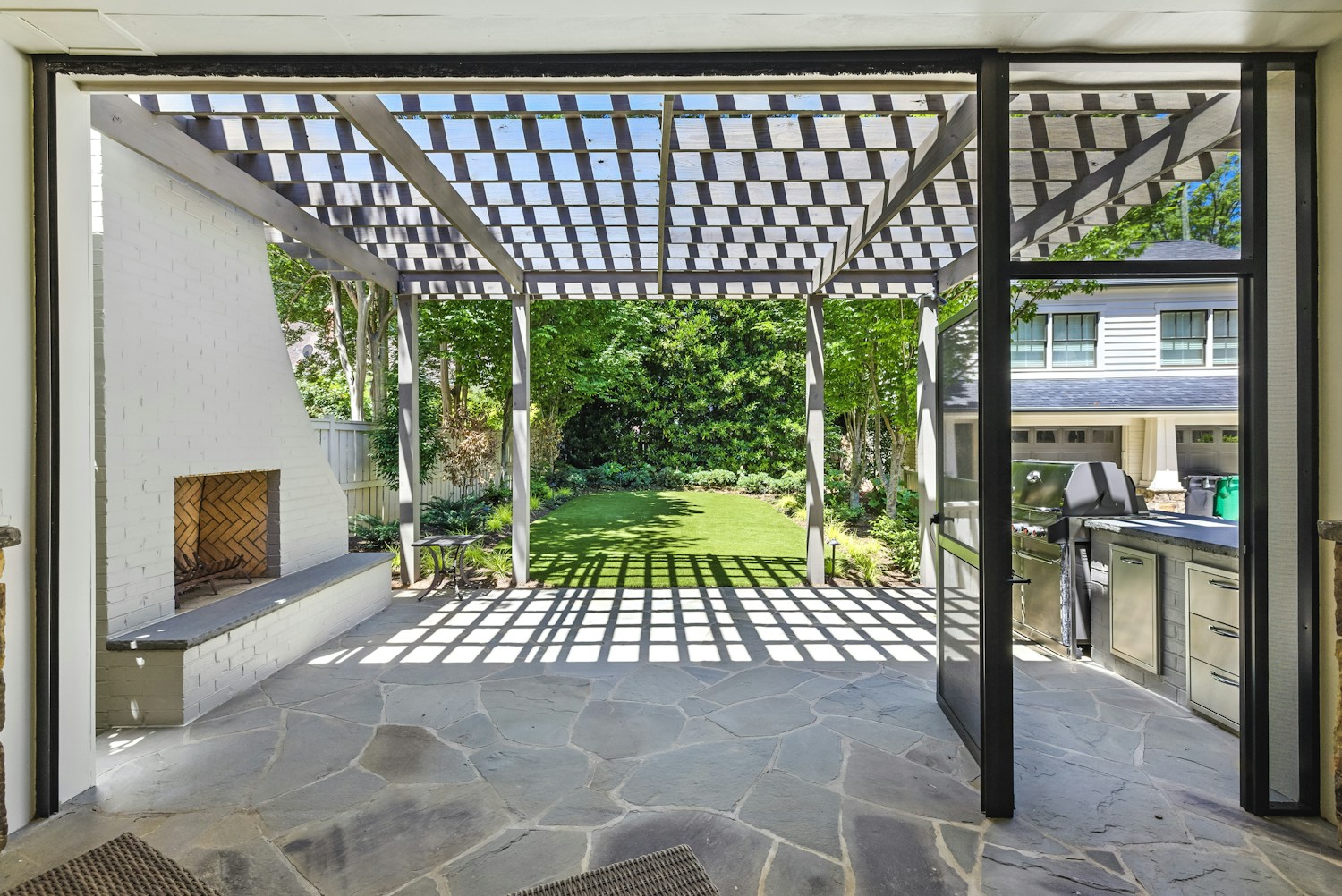 Covered patio with a louvred pergola, outdoor fireplace and garden view